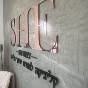 שילוט לוגו תלת מימדי בגוון רוז גולד ושחור על קיר בטון בכניסה לקליניקת יופי
