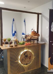 עמדת שף 120 ס"מ מעץ עם תליה עליונה מקורות אקליפטוס ולוגו מואר בחזית, ערוכה עם לחמים, ירקות ורטבים באירוע
